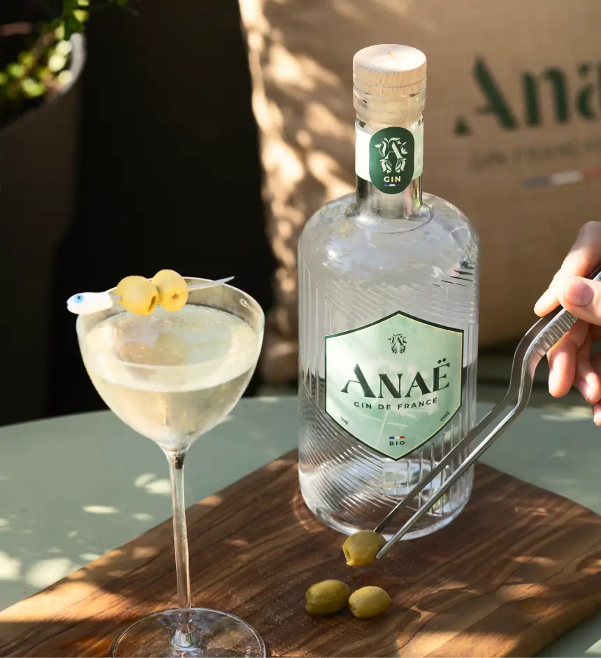 Cocktail au gin Anaë bio avec olives, bouteille de gin de France en arrière-plan