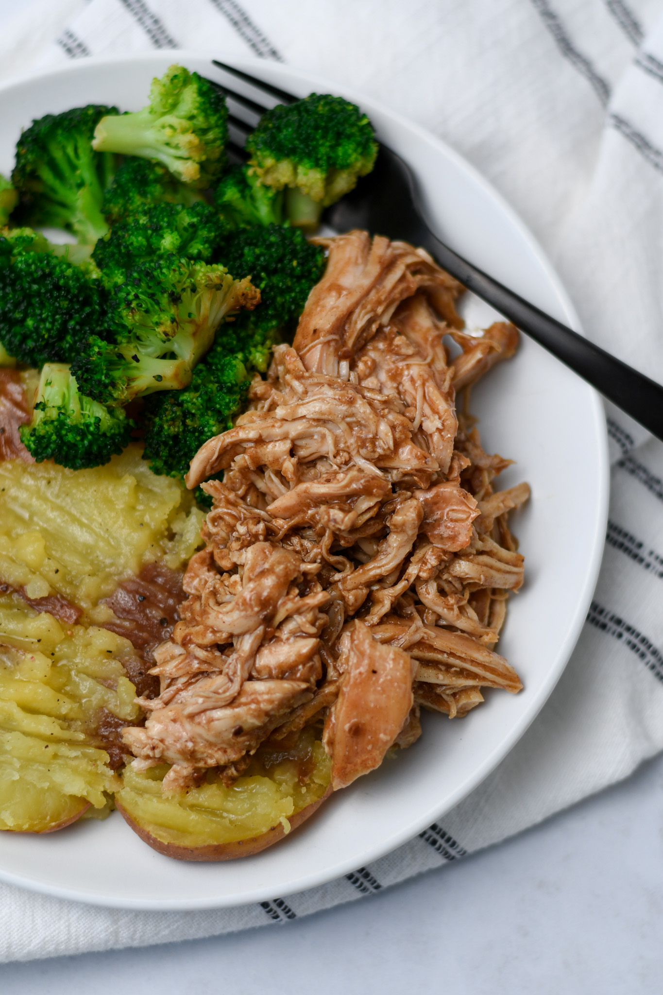 Shredded teriyaki chicken with broccoli and potatoes on a white dinner plate