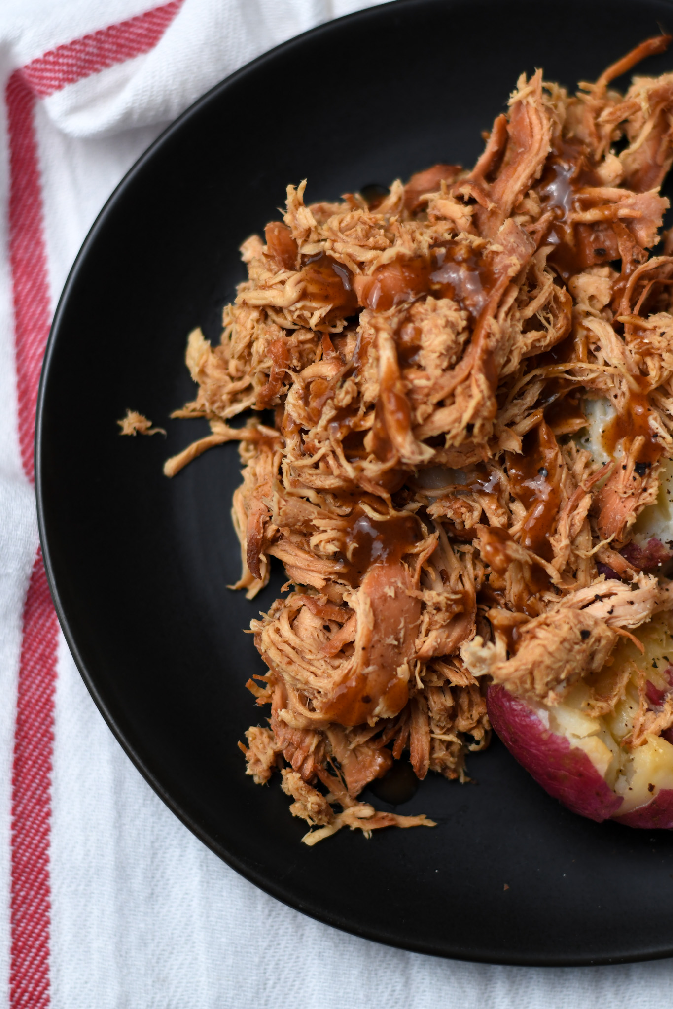 shredded teriyaki chicken on a black plate with red potatoes