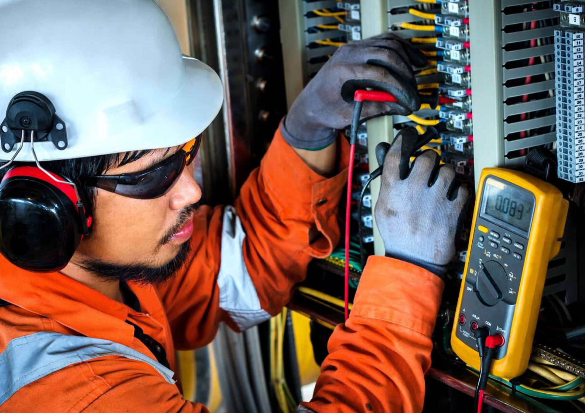 The electrician wearing safety gears is using a multimeter to identify the measurement of the electricity