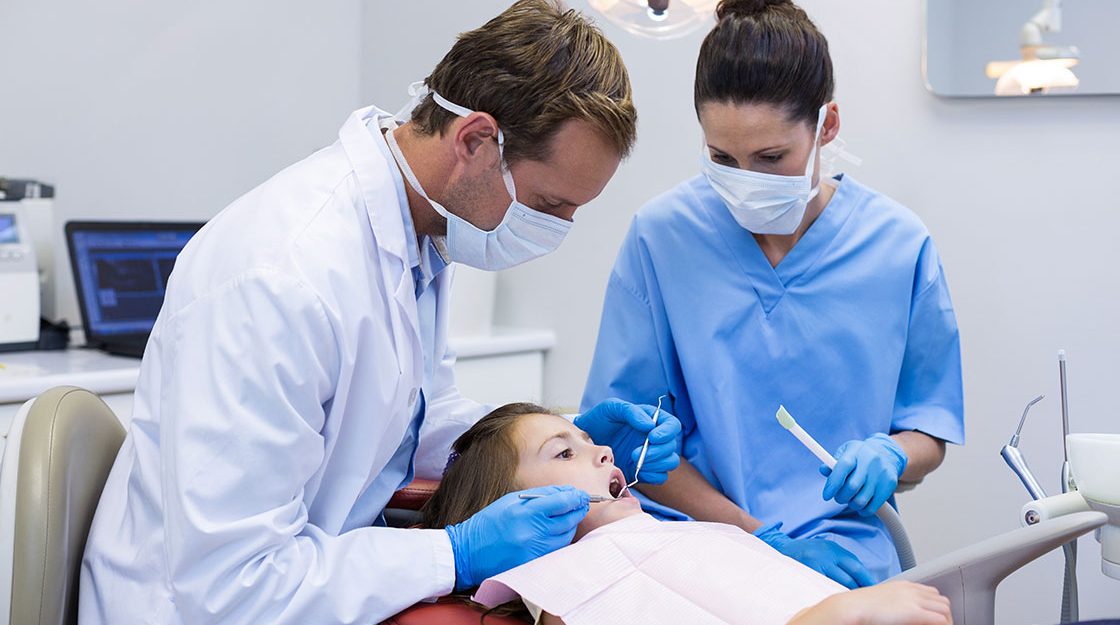 Certified Dental Assistants wearing scrubs, masks and gloves conducts a thorough check-up of a patient's teeth