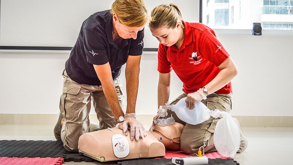 Two individuals are performing CPR on a mannequin as part of a basic life support training