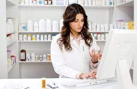 A female pharmacy technician holding medicine while typing on a white keyboard in front of a white computer