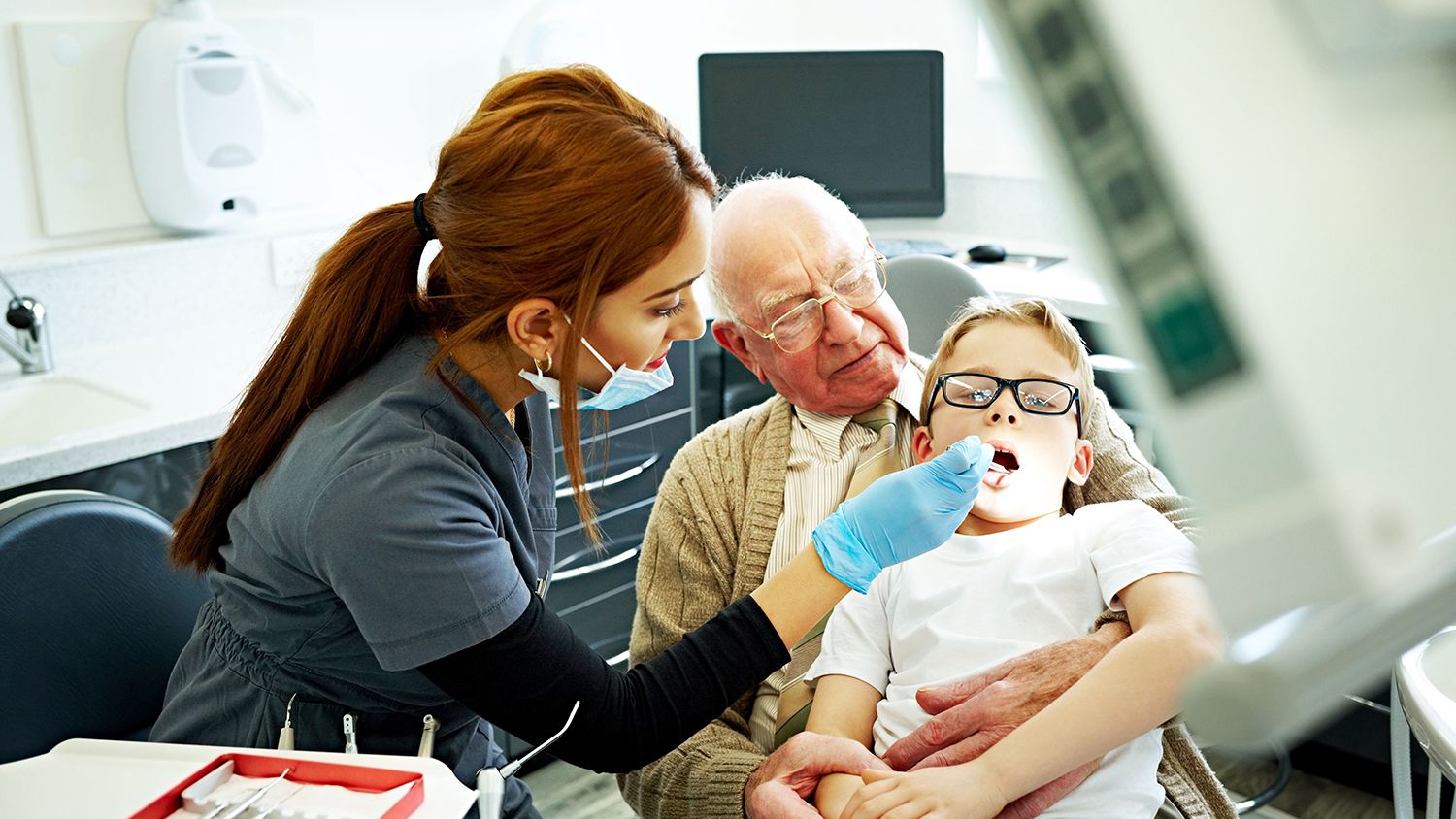 Dental Assistants dressed in scrubs and equipped with mask and gloves, perform a comprehensive examination of a patient's teeth