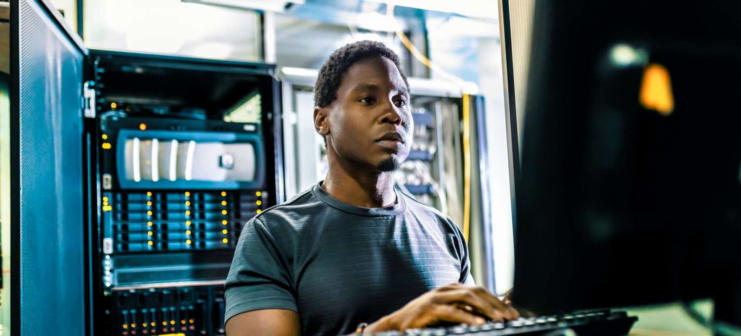 CompTIA A+ certified, sitting in front of a laptop and working on it while there are computer or IT-related hardware in the background.