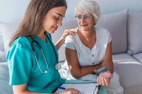 Patient care technician recording the blood pressure of her patient using the wrist blood pressure monitor