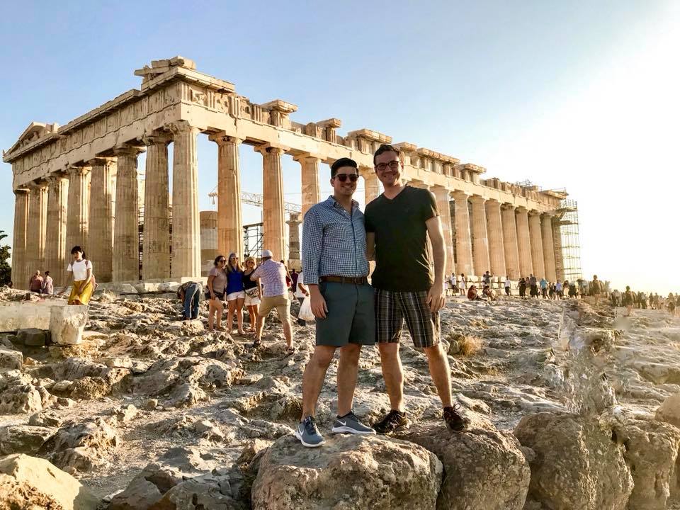 Two men standing on rocks outside the Acropolis in Athens, Greece.