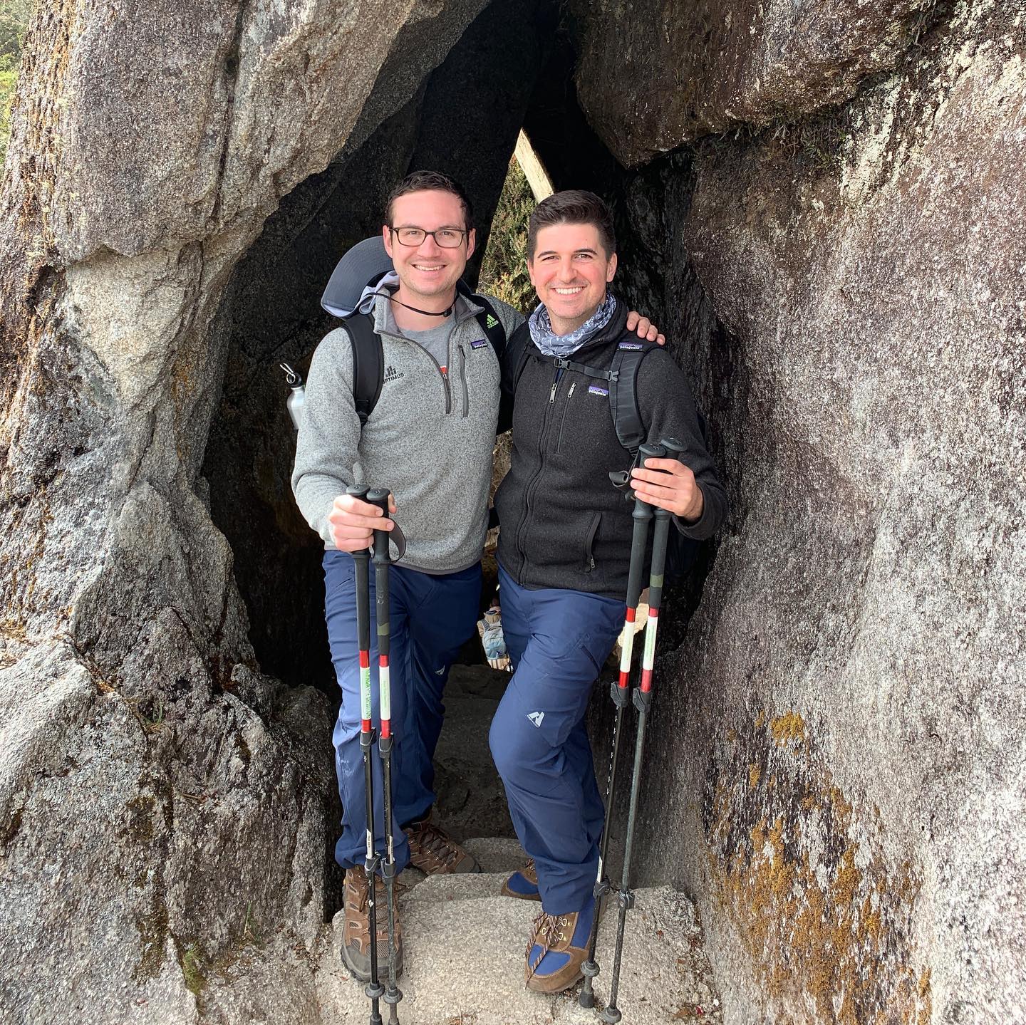 Two men standing at the entrance to a cave with hiking equipment.