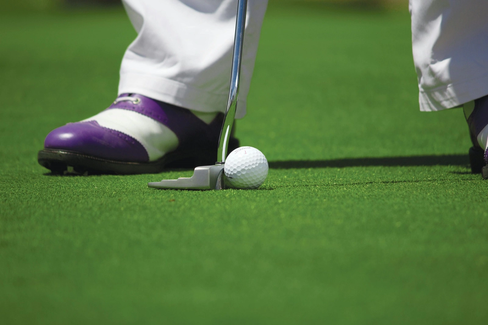 A golf ball on the grass near the player's legs and golf stick