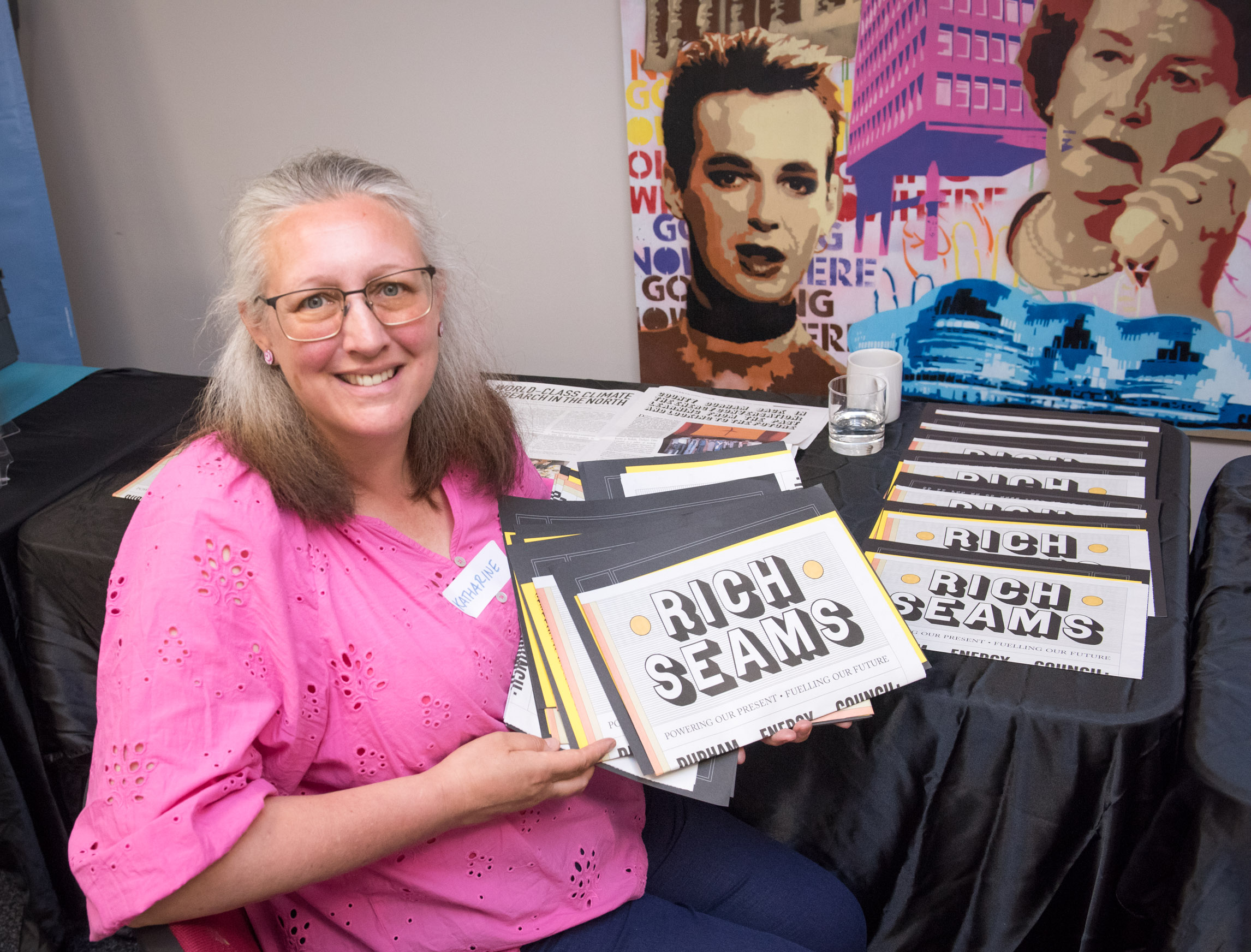 Woman holding up group publication called Rich Seams from Threads in the Ground