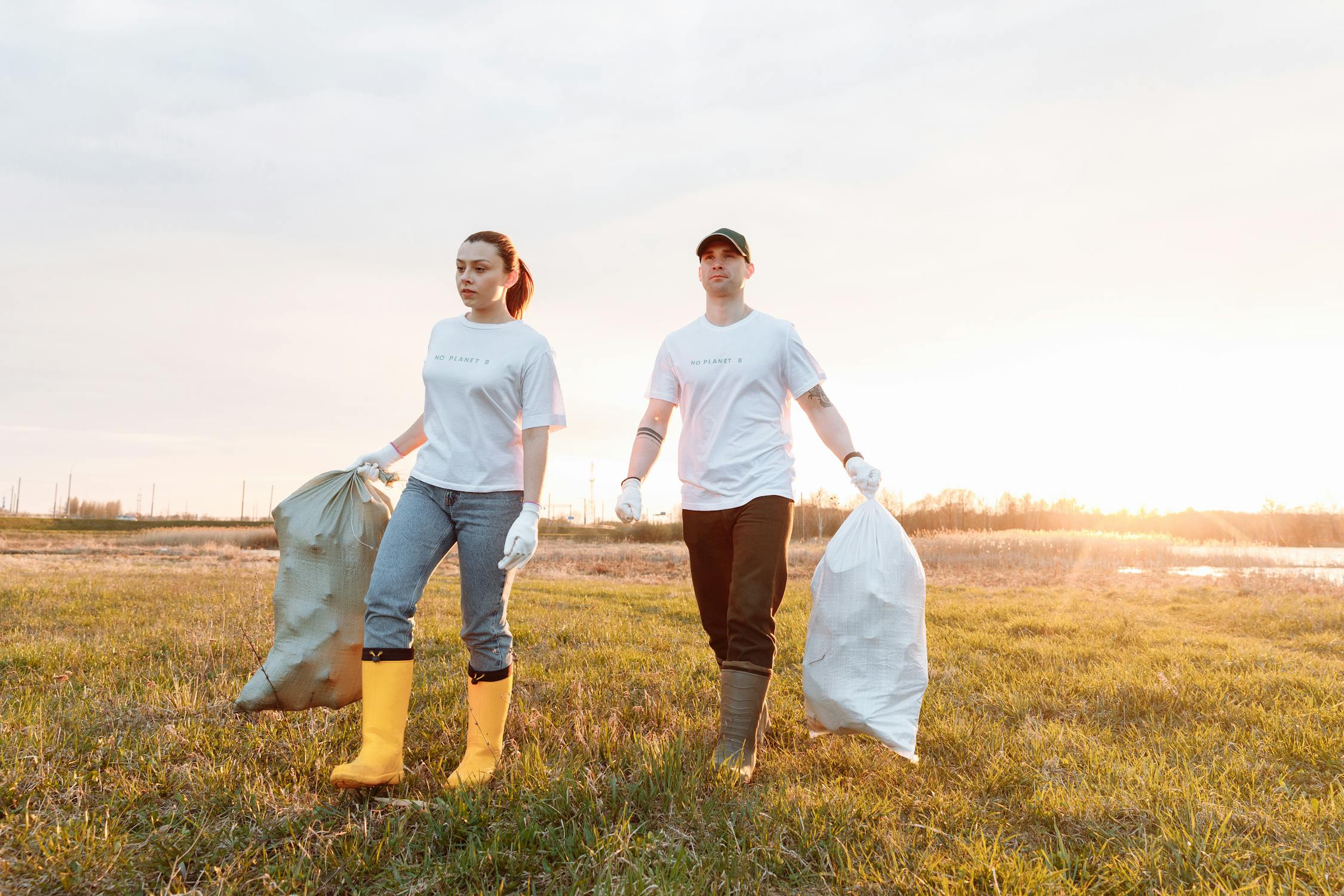 Two people in white tops in welly boots and holding large bags of rubbish