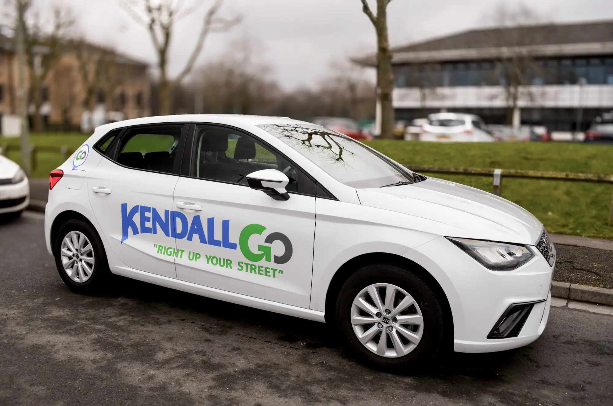 White car parked on street with 'KENDALL GO Right Up Your Street' logo on the side.