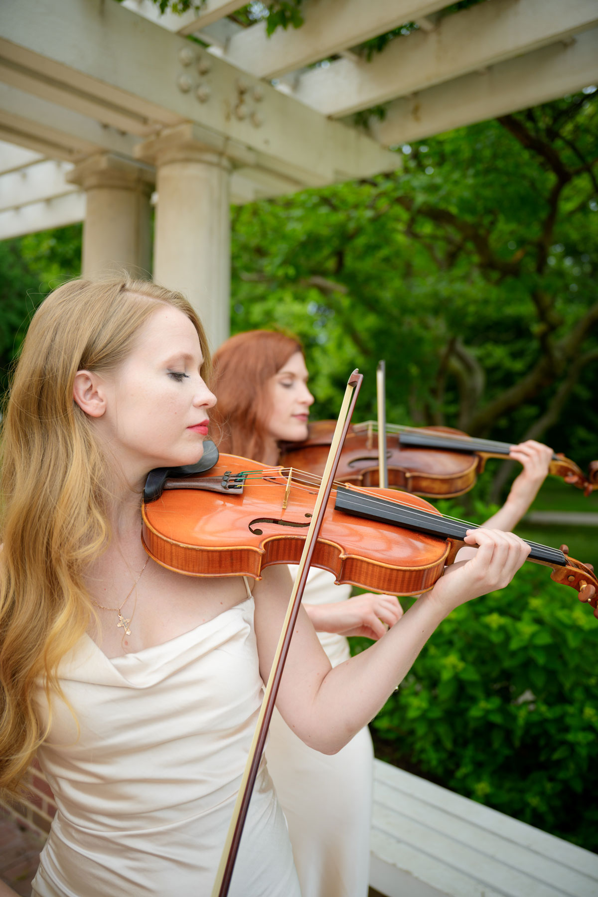 Violinists performing live string music during an outdoor wedding ceremony