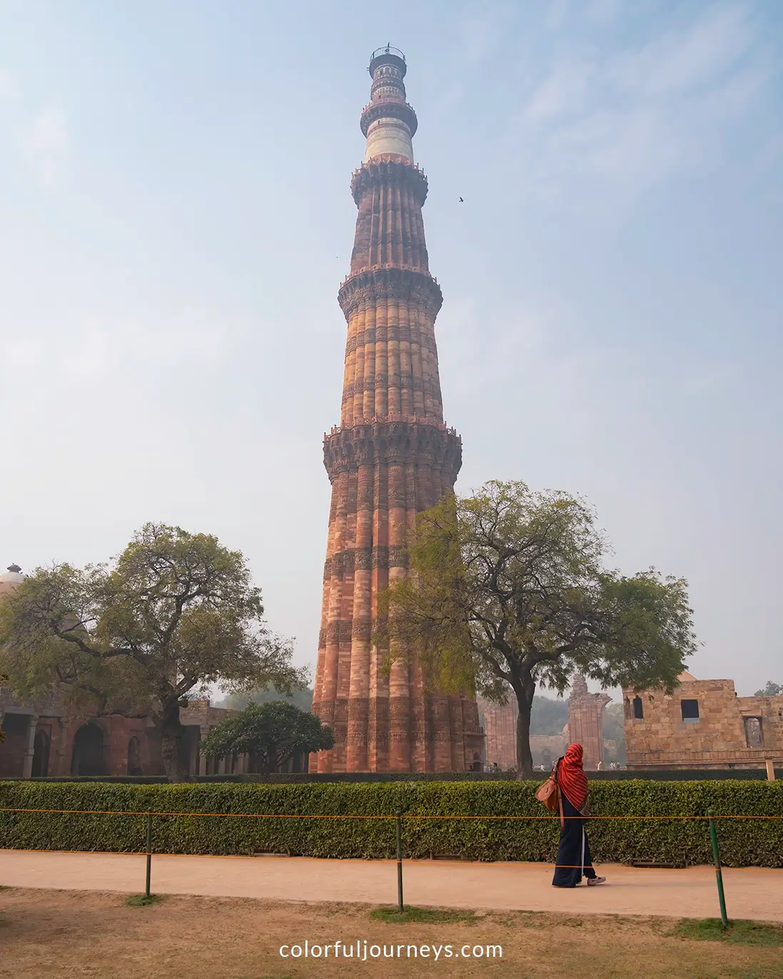 A woman wearing a red hijab walks in front of the Qutub Minar in Delhi, India