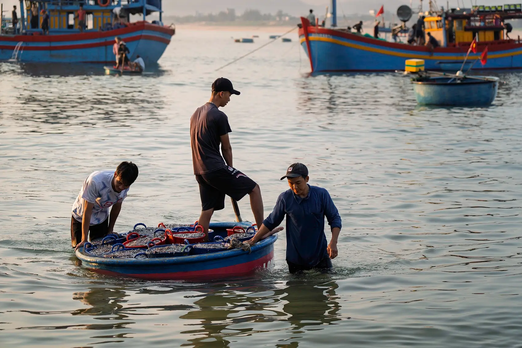 Men navigate a coracle boat filled with fish in Xuan Hai, Vietnam