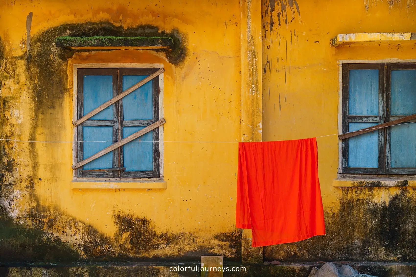 An orange monk robe hangs to dry in front of a yellow wall
