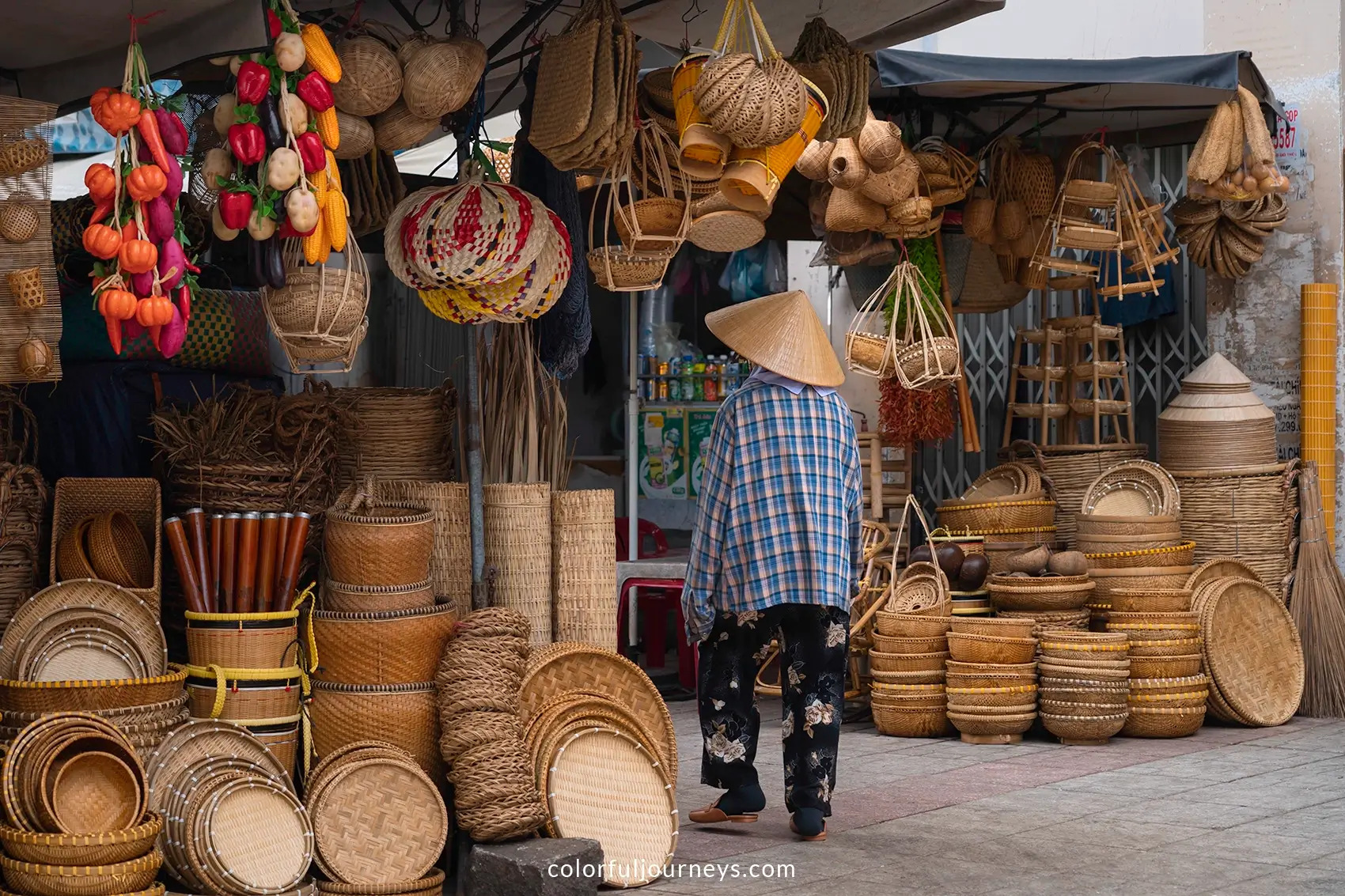 A woman wearing a conical hat walks along woven baskets at a market in Vietnam