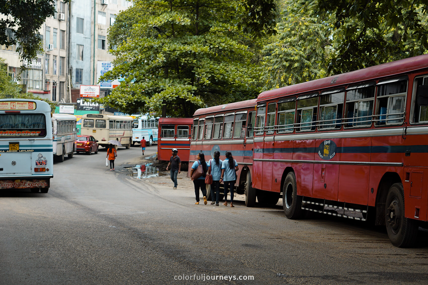 Students walk in front of a red bus in Kandy, Sri Lanka.
