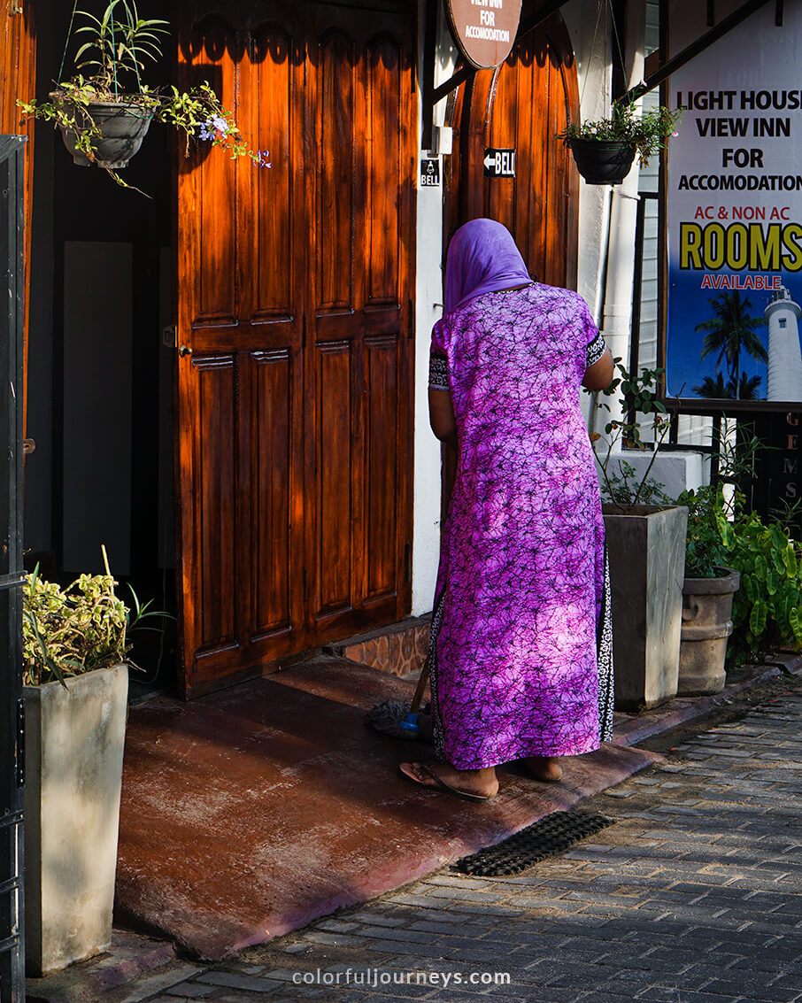 A woman dressed in a purple saris sweeps the street. 