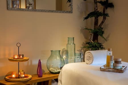 Table de massage avec serviette, soins, bougies allumées et plante, ambiance détente et bien-être.