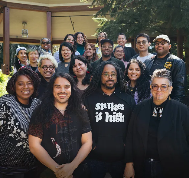 A Black woman sitting, waving to others sitting around her in a black-and-white photo