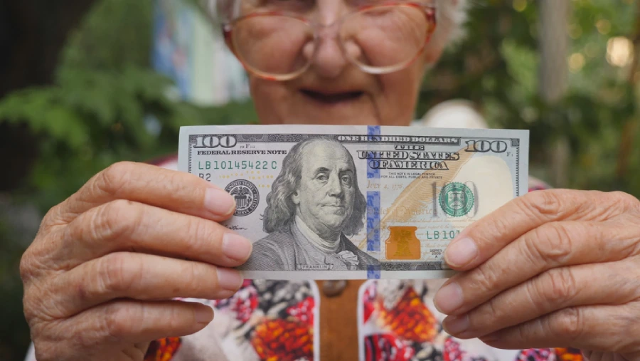 Old woman in eyeglasses showing bill of one hundred dollar into camera