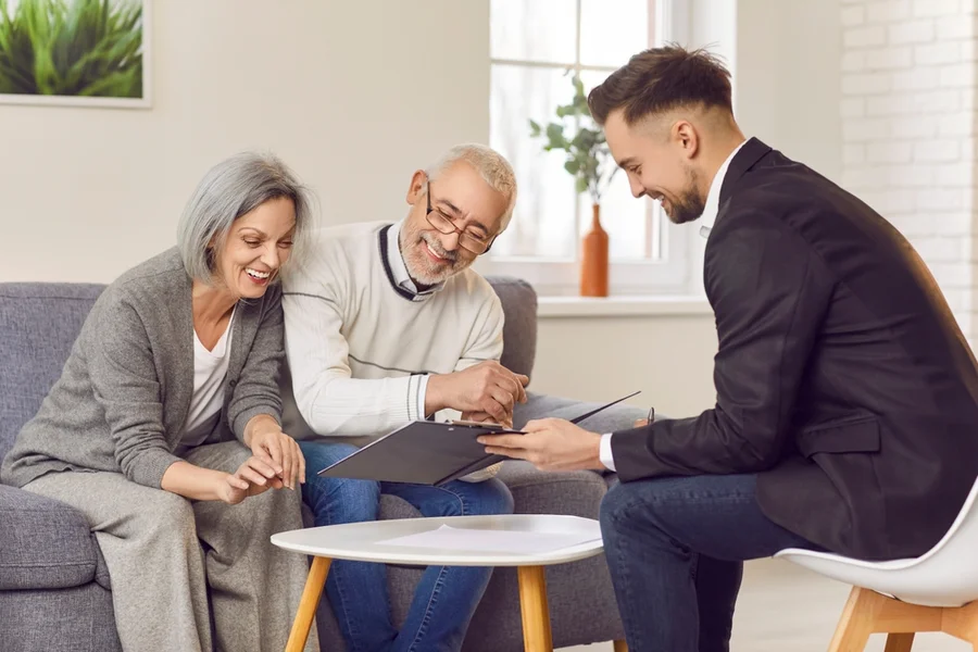 Gray-haired happy smiling senior couple sitting on sofa having consultation with a male financial advisor