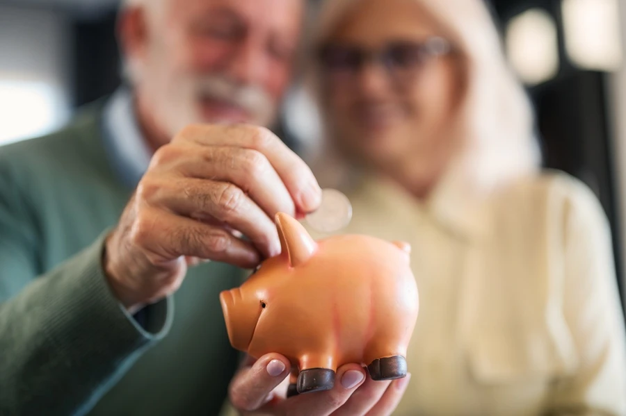 Senior couple putting coin into piggy bank