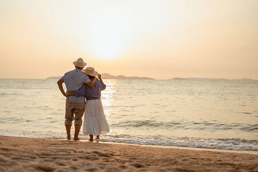 A retired couple standing on the beach looking into the sunset.