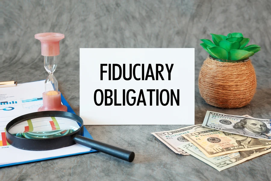 Fiduciary Obligation is written in a document on the office desk with office accessories, money, diagram and magnifier