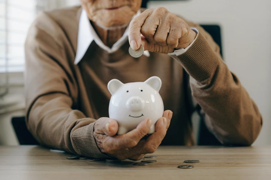 old man hand putting money coins in a piggy bank