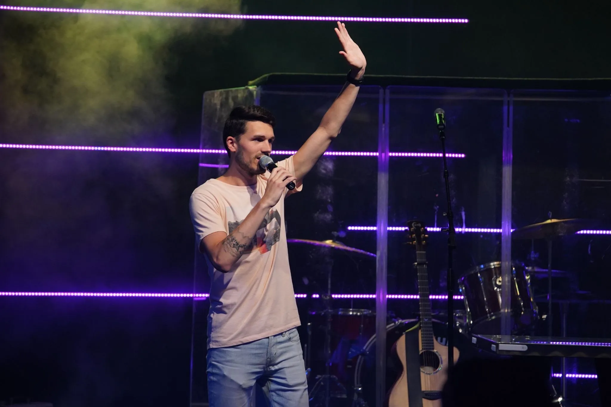 An image capturing the moment of Youth Pastor Ryan Allen during a live worship session, with their hand raised in a gesture of worship or praise.
