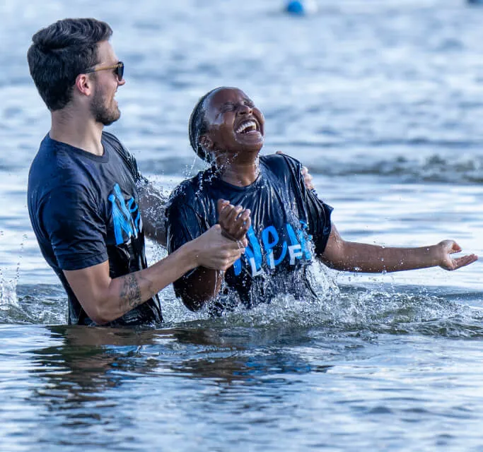 An image showing a reach Church Pastor performing the sacrament of baptism on a woman in the waters of a river.