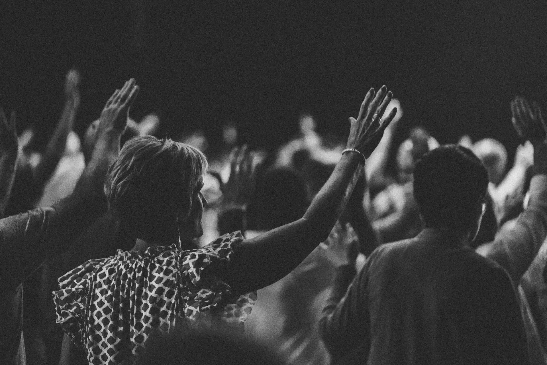 An image depicting a man with their hands raised in a gesture of worship or praise, while attentively listening to a worship service.
