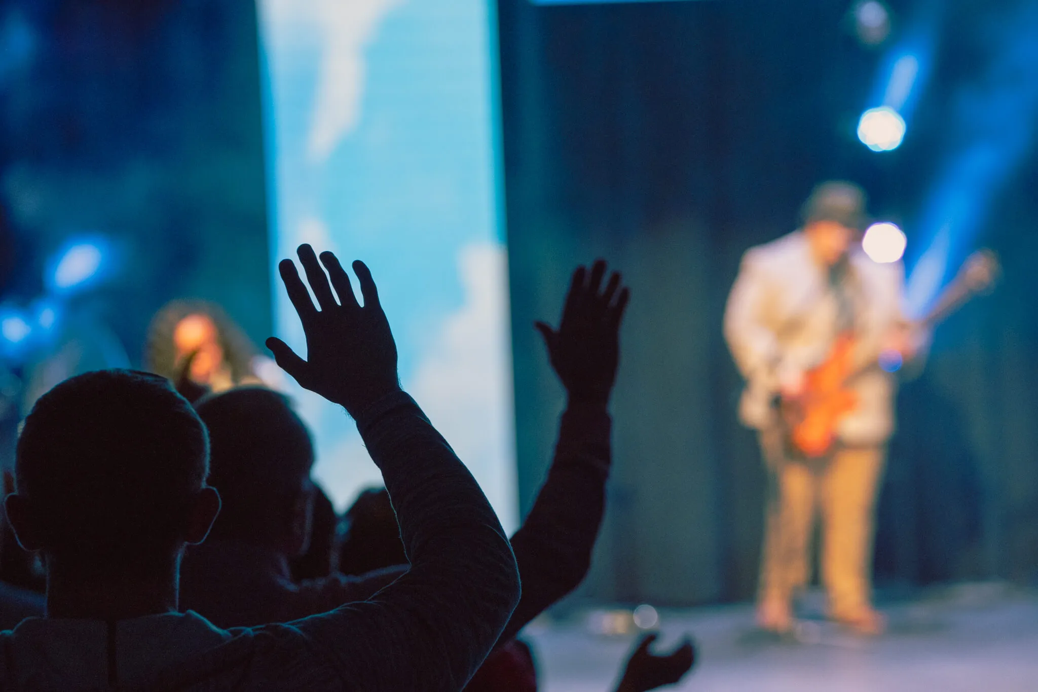 An image depicting a man with their hands raised in a gesture of worship or praise, while attentively listening to a worship service.