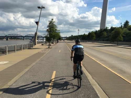 image of a person on a bike on a cycle track at the missississippi riverfront and gateway arch. Shows the cycle track elevated to the same height as the sidewalk