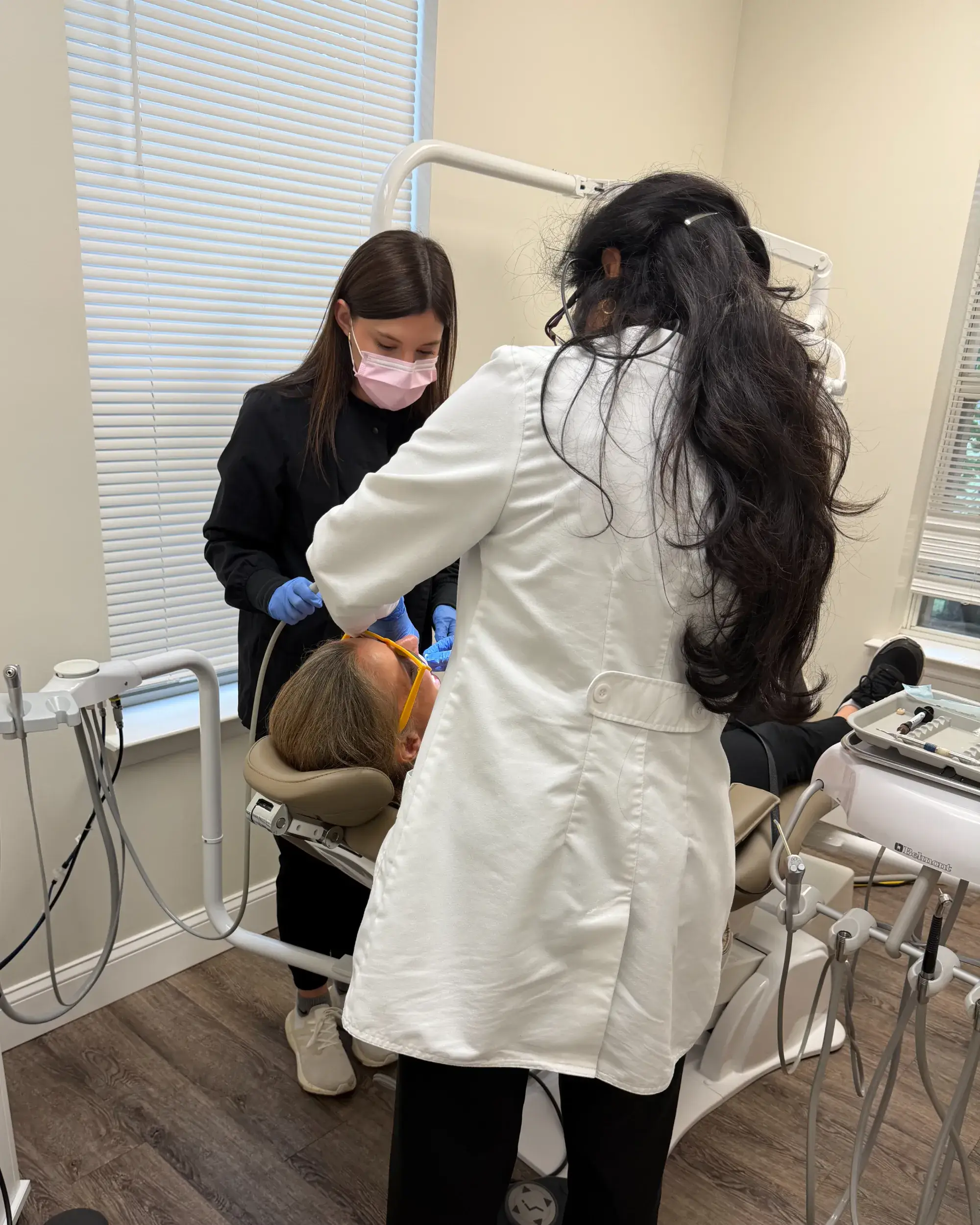 A dentist and an assistant examine a patient's teeth in a dental office.