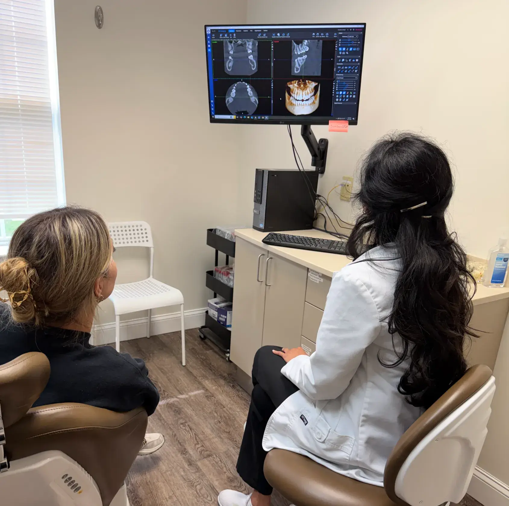 A dentist shows a patient dental scans on a computer in an office.