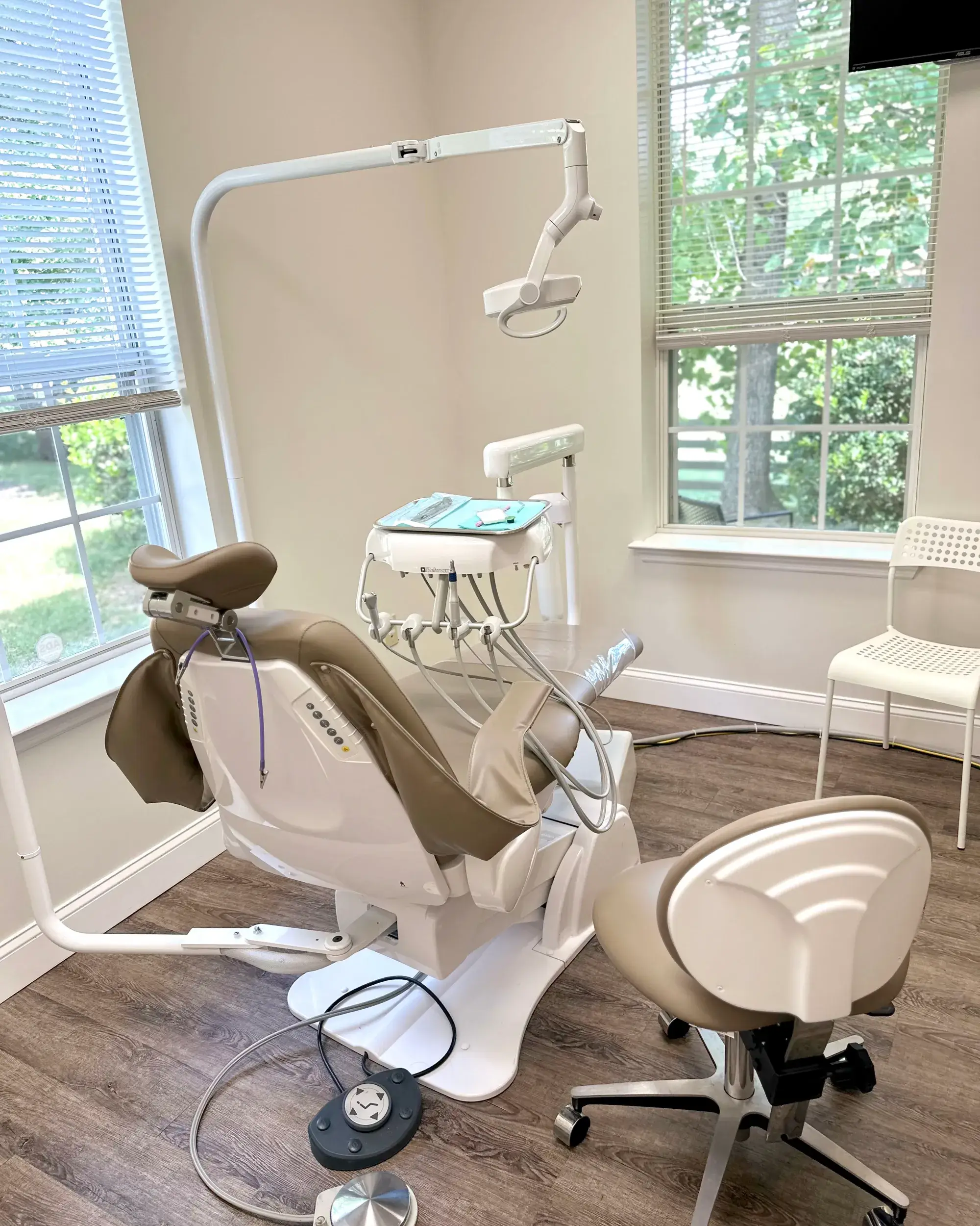 Dental examination room with a dentist chair, equipment, and windows with blinds.