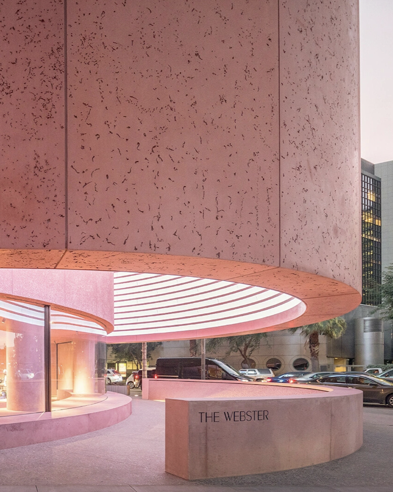 Curved modern building entrance with pink lighting and a concrete sign reading 'THE WEBSTER'.