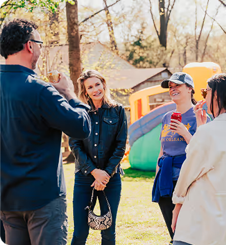 Diverse group of people serving themselves food from a buffet-style table filled with various dishes and a pitcher of iced tea in a communal dining setting.