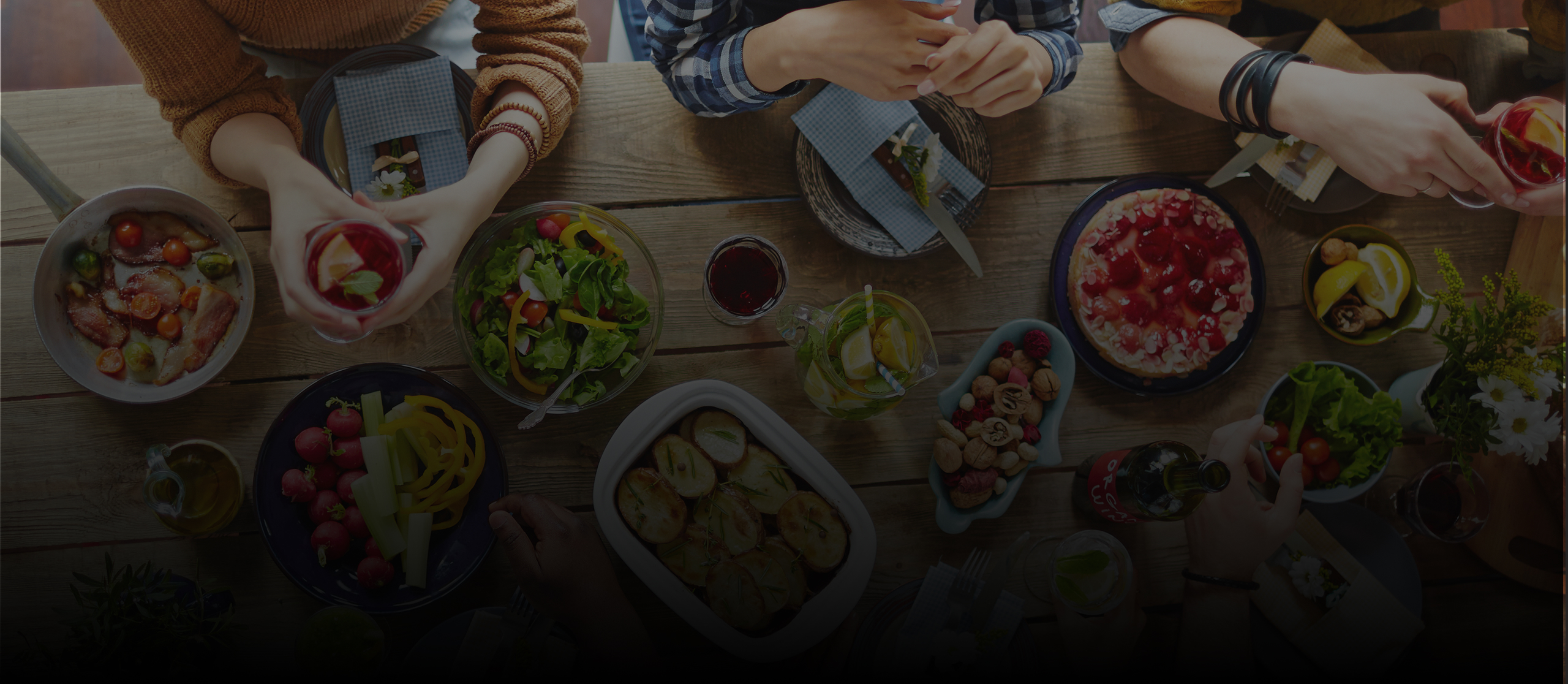 Top view of people toasting with drinks over a table with salad, avocados, rolls, and tomatoes; next to a group of four women smiling and chatting around a dinner table with a cake and flowers.