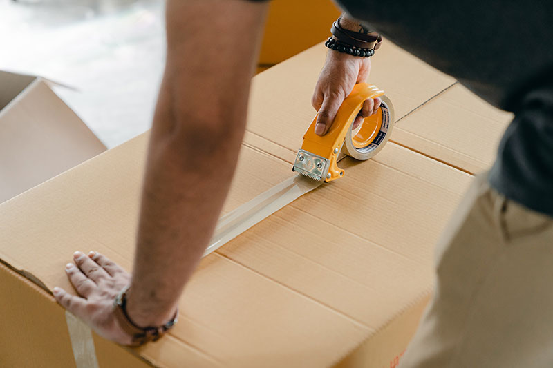 A man sealing a cardboard box with sticky tape