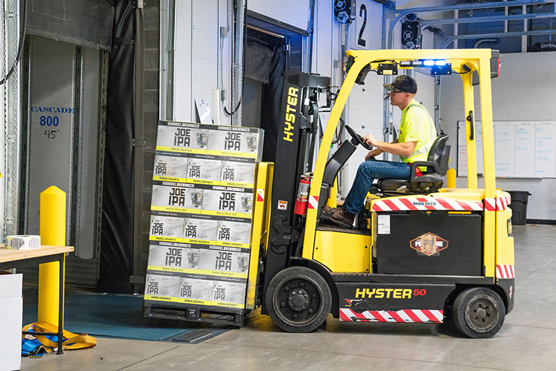 A forklift carrying a crate of boxes driving into a factory