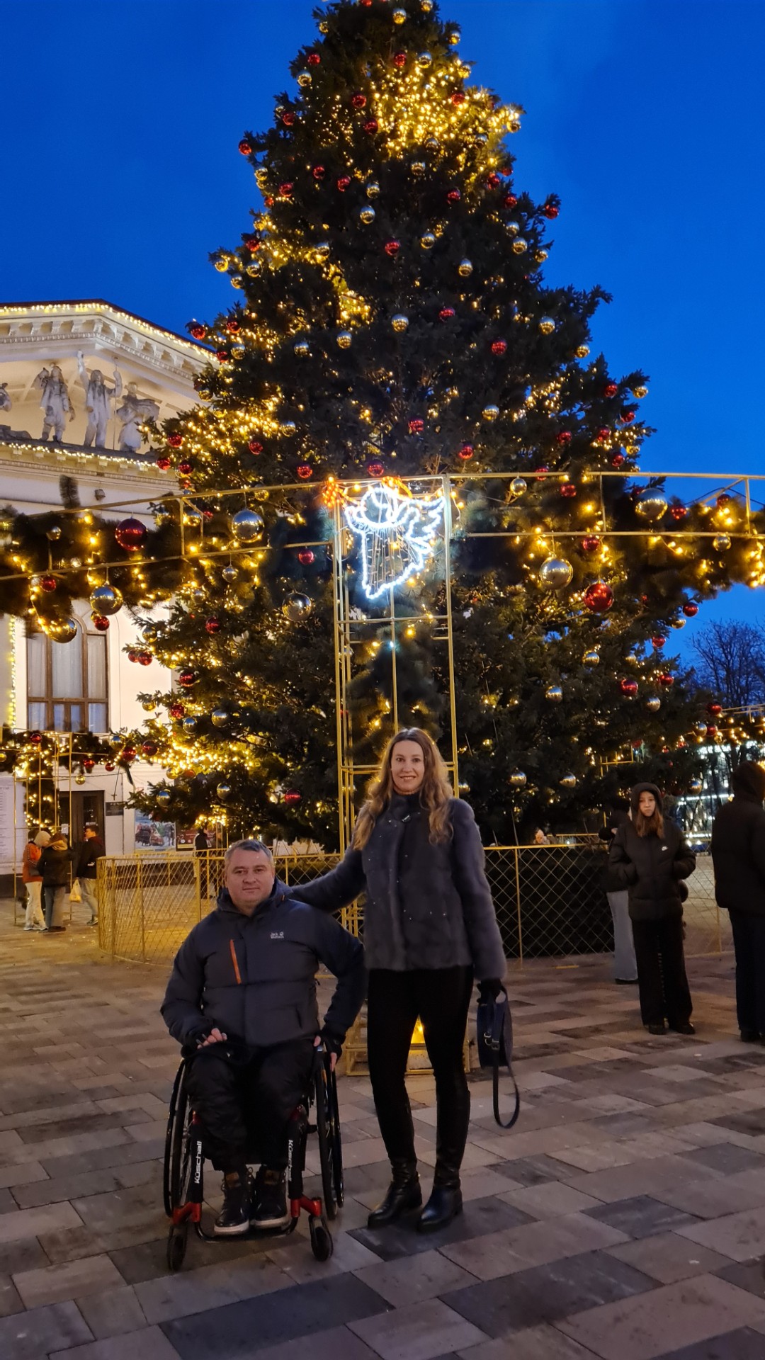 Volodymyr og kona er foran et dekorert juletre utendørs, som lyser opp den mørkeblå vinterhimmelenn