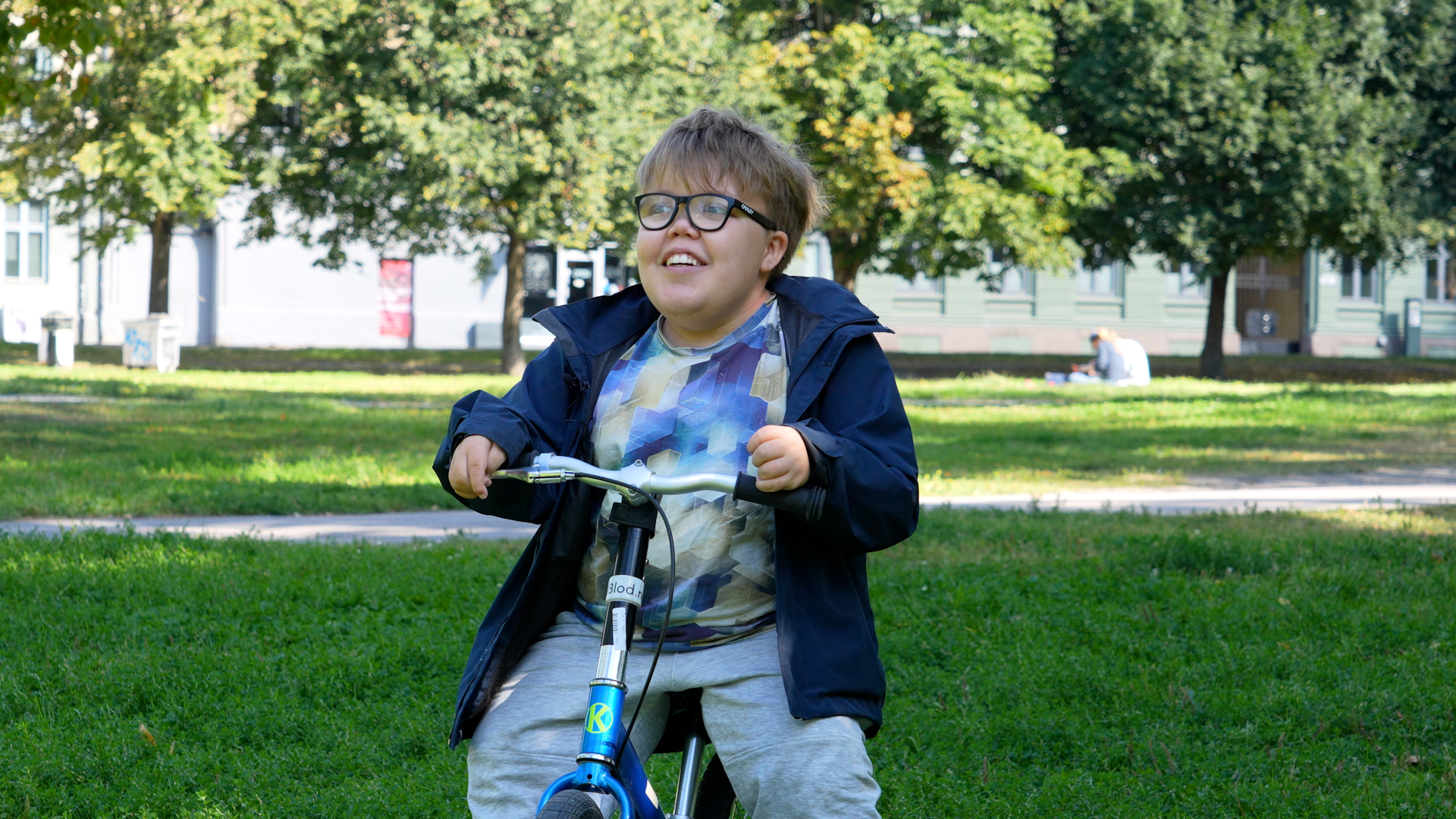 Trygvekikker smilende ut i luften i Sofienbergparken mens han står i bekjent posisjon på sykkelen sin.  