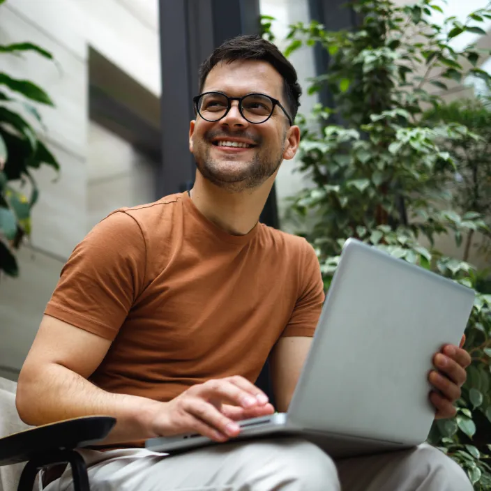 Mitarbeiter arbeitet lächelnd mit einem Laptop in einer modernen, begrünten Büroumgebung.