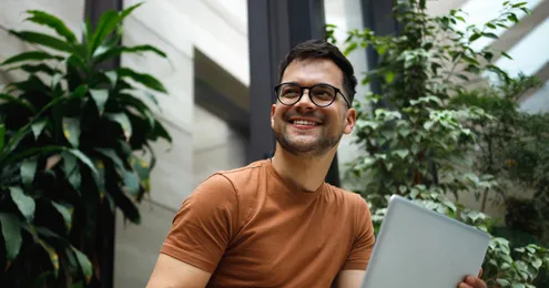 Mitarbeiter arbeitet lächelnd mit einem Laptop in einer modernen, begrünten Büroumgebung.