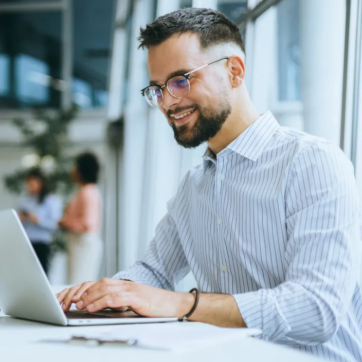 Ein Mann in einem Hemd arbeitet an einem Laptop, während er an einem Schreibtisch sitzt