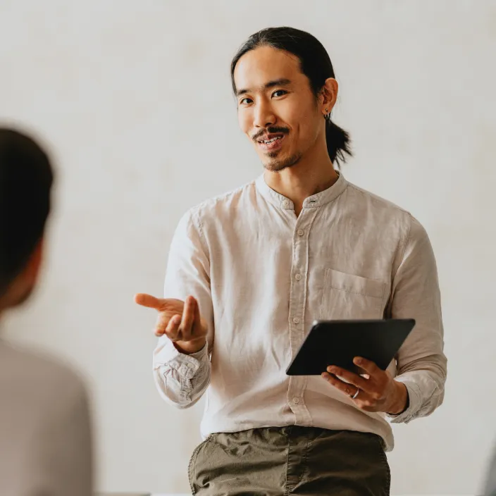 Junger Mann hält eine Präsentation mit einem Tablet und gestikuliert dabei.
